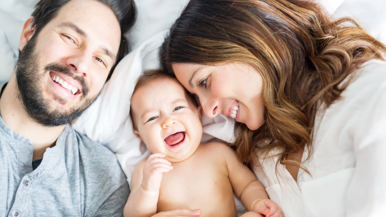 Lächelndes Baby liegt zwischen seinen Eltern.