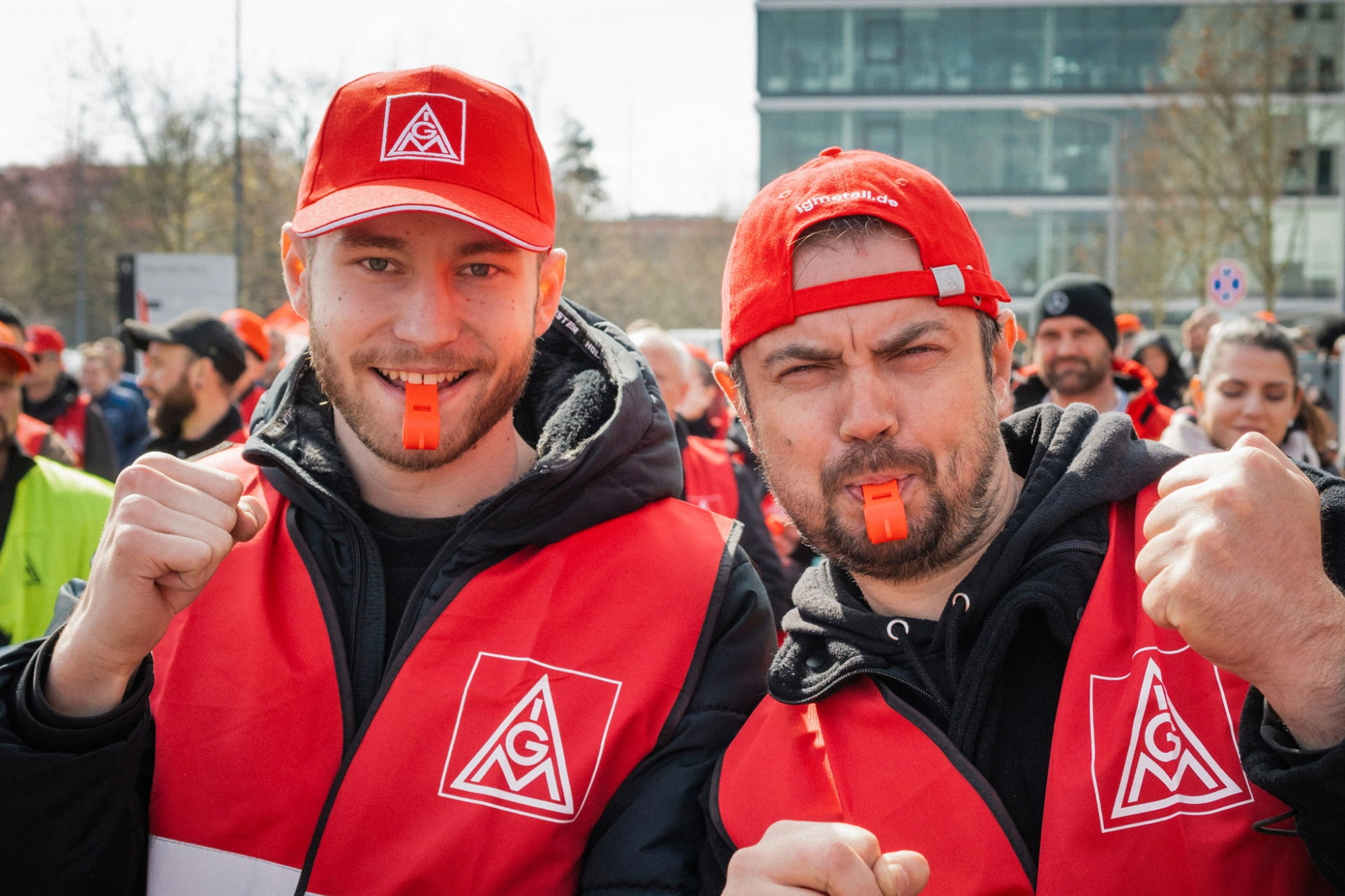 Zwei Beschäftigte mit Trillerpfeife, roter Kappe und Weste beim Warnstreik in der Kfz-Tarifrunde in Nürnberg