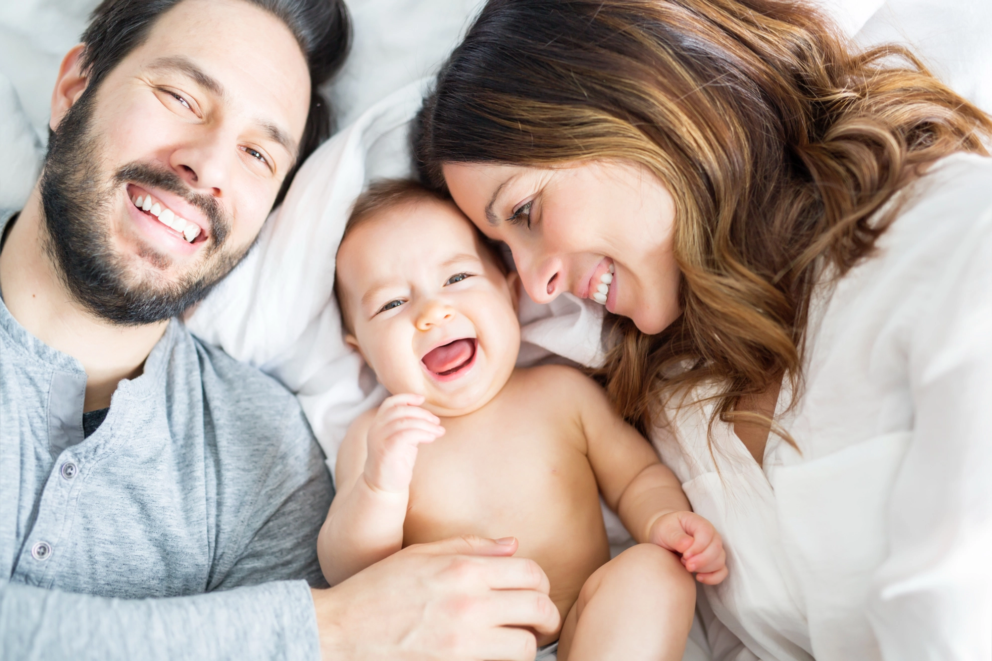 Lächelndes Baby liegt zwischen seinen Eltern.